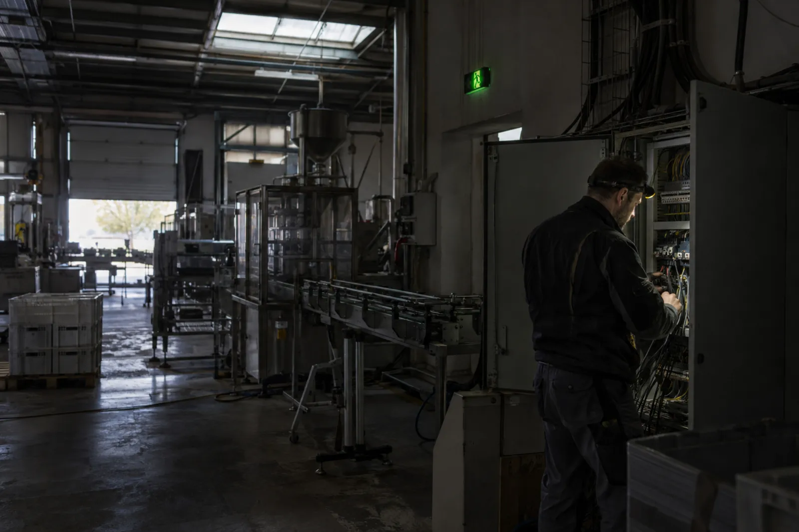 Elektrikář s čelovkou kontroluje rozvaděč v zastavené výrobní hale bez proudu